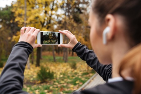 Close up of fitness woman in earphones taking a photo while jogging at the parkの写真素材