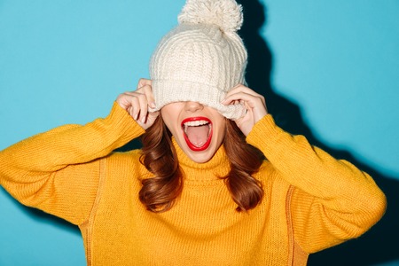 Portrait of a cheery young girl dressed in winter hat laughing isolated over blue backgroundの写真素材