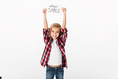 Portrait of a cheery little girl holding sheet of paper with an inscription Always smile isolated over white backgroundの写真素材