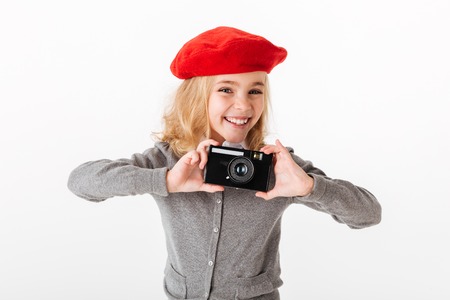 Portrait of a smiling little schoolgirl dressed in uniform taking a shot with a retro camera...