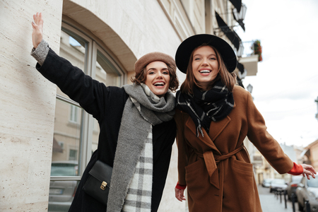 Portrait of two cheery girls dressed in autumn clothes walking on a city streetの写真素材