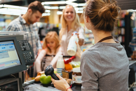Cheerful family standing at the cash counter buying groceries at the supermarketの写真素材