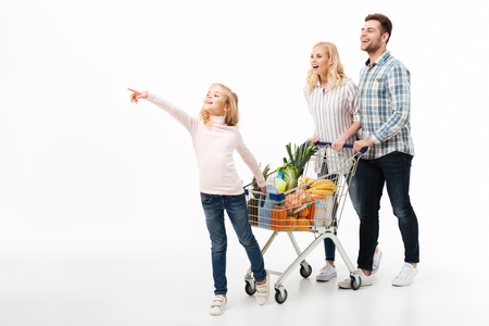 Full length portrait of a young family walking with a shopping trolley full of groceries isolated over white backgroundの写真素材