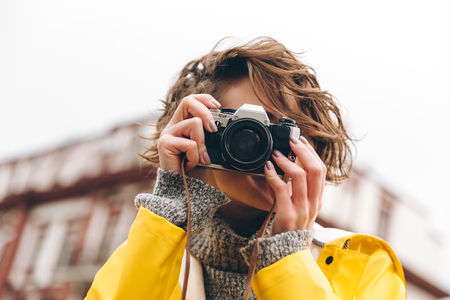 Photo of gorgeous young lady photographer dressed in raincoat walking outdoors holding camera.の写真素材
