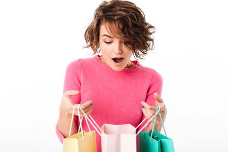 Image of pretty young woman standing isolated over white background looking aside holding shopping bags.の写真素材