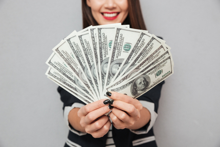 Cropped image of smiling asian business woman showing money at the camera over gray backgroundの写真素材