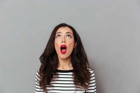 Portrait of a shocked girl looking up at copy space with open mouth isolated over gray backgroundの写真素材