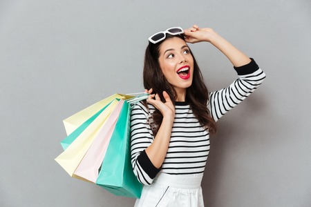 Portrait of a cheerful woman holding shopping bags and looking away isolated over gray backgroundの写真素材