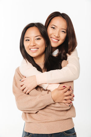 Picture of two asian pretty smiling ladies sisters hugging with each other. Looking camera.の写真素材