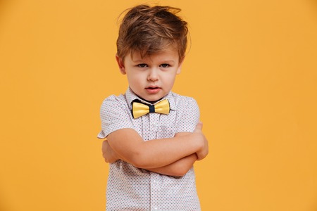 Portrait of a sad little boy child standing isolated over yellow background. Looking aside.の写真素材