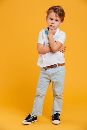 Picture of serious concentrated little boy child standing isolated over yellow background. Looking camera.の写真素材