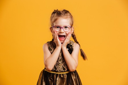Photo of shocked little girl child standing isolated over yellow background. Looking camera.の写真素材