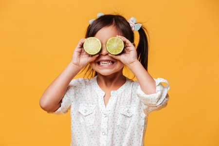 Image of little cute girl child standing isolated over yellow background. Covering eyes with lime.の写真素材