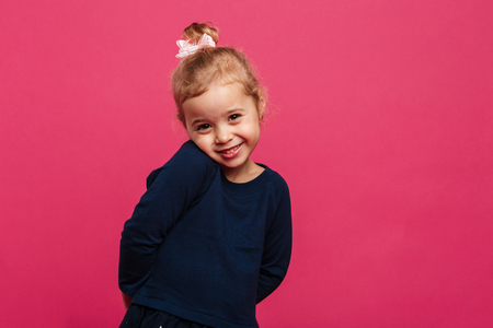 Shy young blonde girl posing in studio and looking at the camera over pink backgroundの写真素材