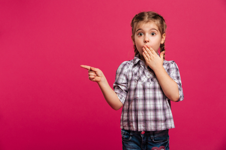 Image of surprised cute little girl child standing isolated over pink background pointing.の写真素材