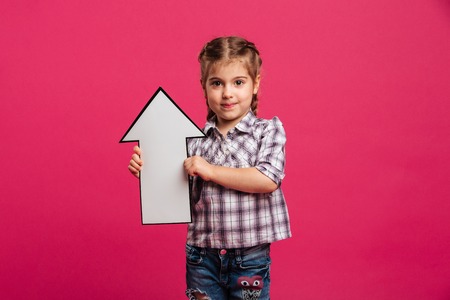 Image of smiling little girl child standing isolated over pink background holding arrow.の写真素材