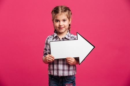Image of smiling little girl child standing isolated over pink background holding arrow.の写真素材