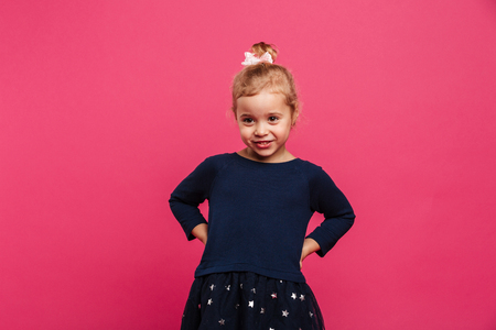 Pretty young blonde girl holding arms on hips and looking aside over pink backgroundの写真素材