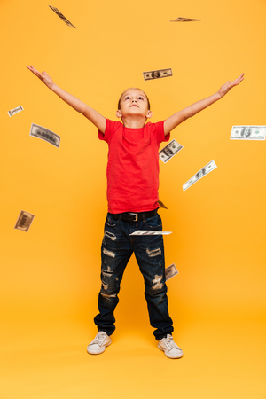 Image of concentrated little boy child standing isolated over yellow background. Looking aside over money.の写真素材