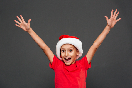 Photo of happy little boy child wearing christmas santa hat standing isolated over grey background. Looking camera.の写真素材