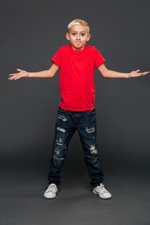 Image of confused little boy child standing isolated over grey background. Looking camera.の写真素材