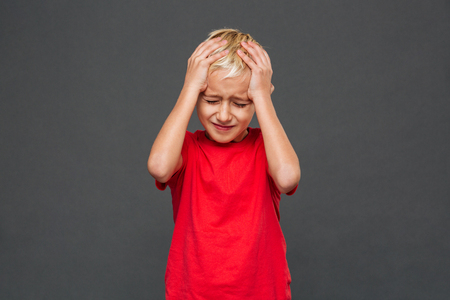 Photo of sad little boy child with headache standing isolated over grey background.の写真素材