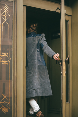 Portrait of a young bearded man dressed in coat enters a door in a cafeの写真素材