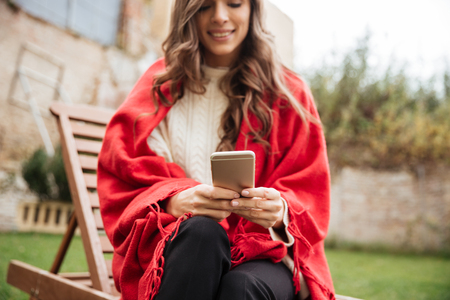 Cropped image of a smiling woman texting on mobile phone while sitting outdoors at the parkの写真素材