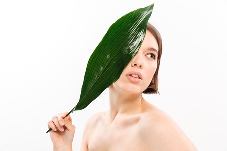 Beauty portrait of a beautiful half naked woman with short brunette hair posing with green leaf isolated over white backgroundの写真素材