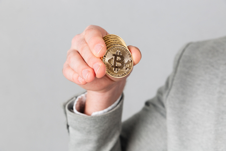 Close up of male hand showing golden bitcoin isolated over gray backgroundの写真素材