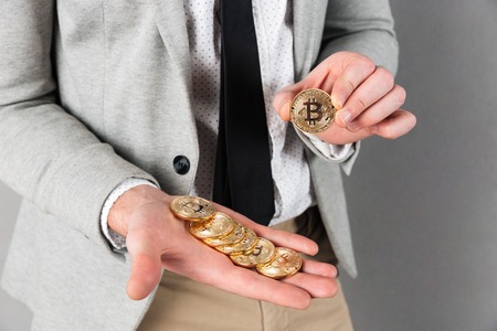 Close up of man holding stack of golden bitcoins on his palm isolated over gray backgroundの写真素材