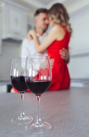 Close up of glasses with red wine on table. Young man and woman hugging in the backgroundの写真素材