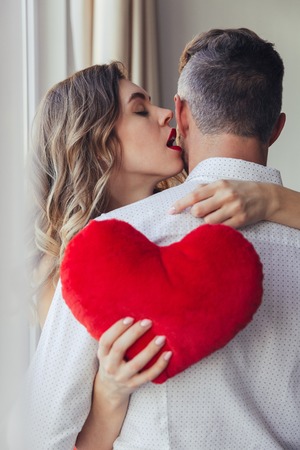 Portrait of a sensual young woman holding her boyfriend and holding toy heart indoorsの写真素材