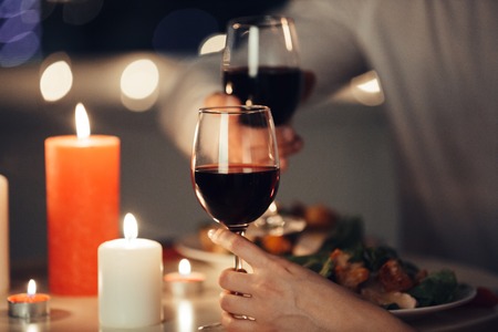 Cropped photo of young lovers having romantic dinner and drinking red wine at homeの写真素材