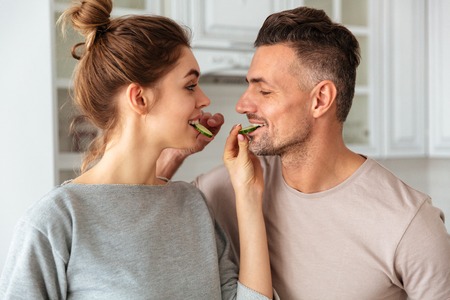 Smiling lovely couple cooks together on kitchen and feeding to each otherの写真素材