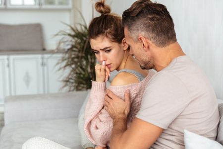 Side view of attentive man sitting on couch and calm down his upset girlfriend which crying at homeの写真素材