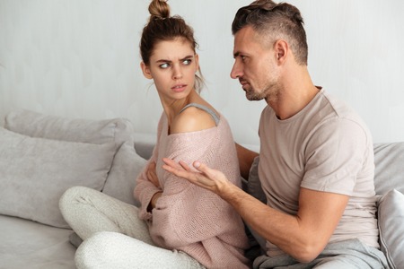 Side view of Careful man sitting on couch and calm down his upset girlfriend at home