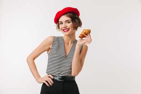 Portrait of a happy woman wearing red beret holding croissant isolated over white backgroundの写真素材