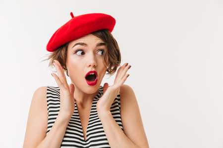 Portrait of a shocked woman dressed in red beret screaming and looking away isolated over white backgroundの写真素材