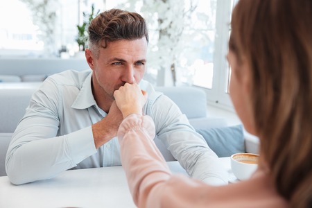 Cropped image of Sensual man in shirt sitting by the table with his girlfriend and kissing her handの写真素材