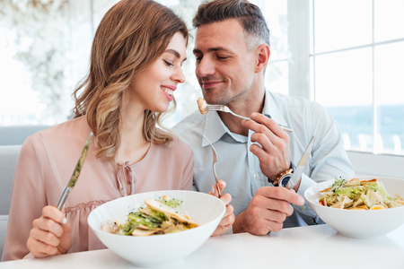 Photo of adult romantic couple having dinner and eating salats while resting city cafe on sunny dayの写真素材