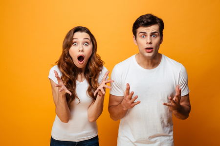 Portrait of a shocked young couple looking at camera isolated over yellow backgroundの写真素材