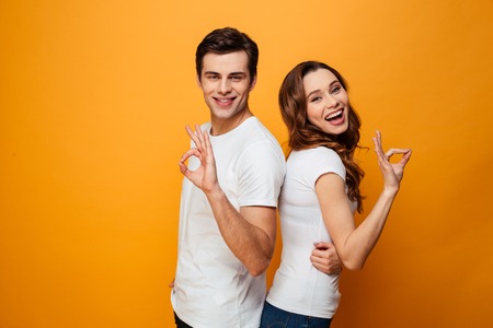 Portrait of a smiling young couple showing ok gesture isolated over yellow backgroundの写真素材