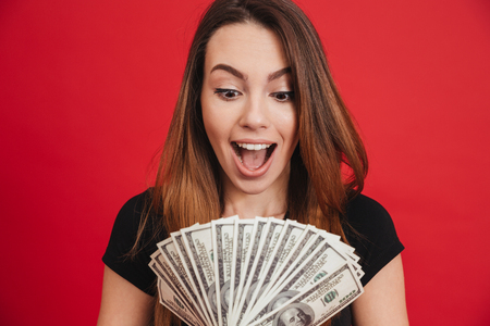 Portrait of a satisfied girl holding bunch of money banknotes isolated over pink backgroundの写真素材