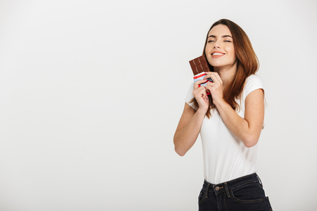 Portrait of a happy young woman holding chocolate bar isolated over white backgroundの写真素材