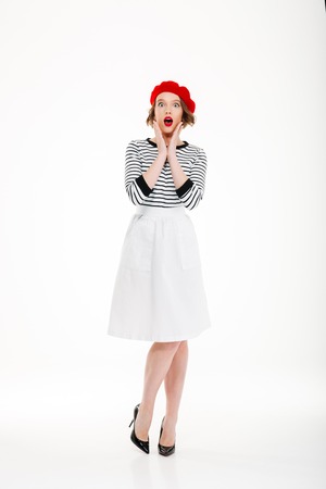 Surprised beautiful lady in red beret looking camera with opened mouth isolated over whiteの写真素材