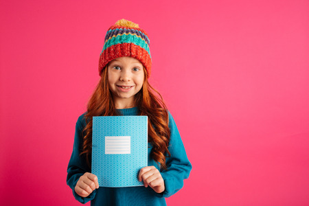 Young beautiful redhead girl showing blue copy book and smiling isolated over pinkの写真素材