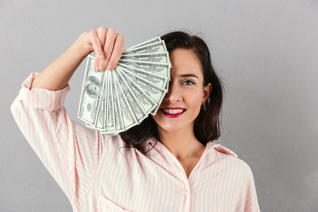 Close up portrait of a cheerful businesswoman showing bunch of money banknotes isolated over gray backgroundの写真素材