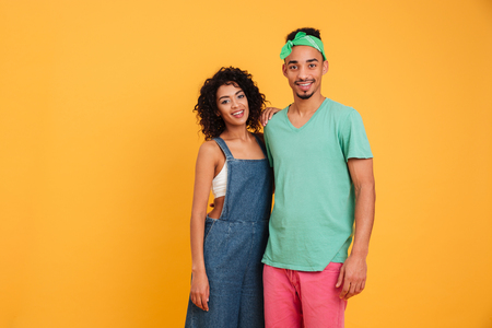 Portrait of a smiling young african couple dressed in summer clothes hugging isolated over yellow backgroundの写真素材