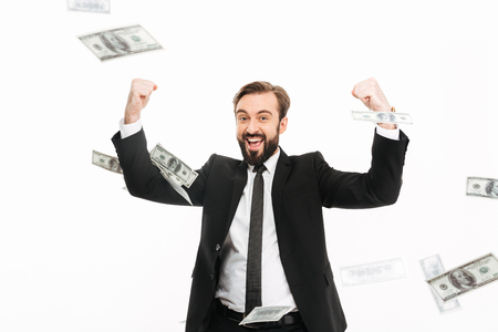 Portrait of happy caucasian man in suit rejoicing his prize while standing under falling dollar banknotes isolated over white backgroundの写真素材